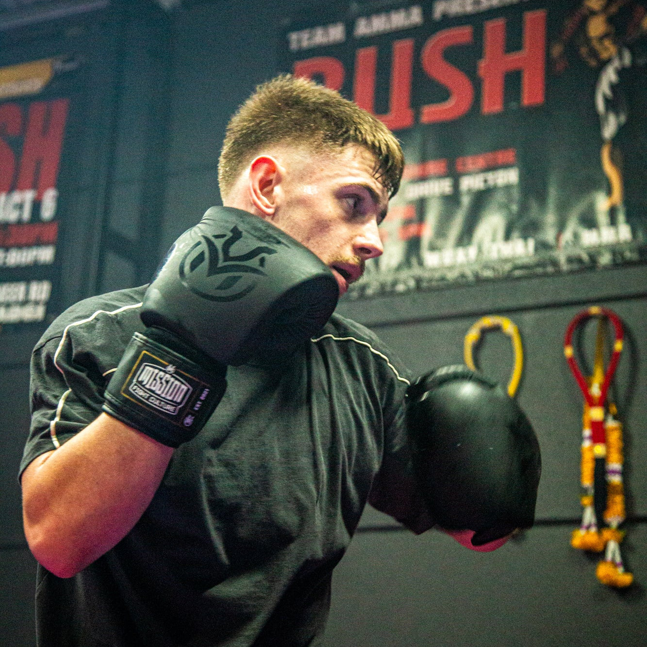 Person wearing boxing gloves in a gym setting with promotional posters on the wall.