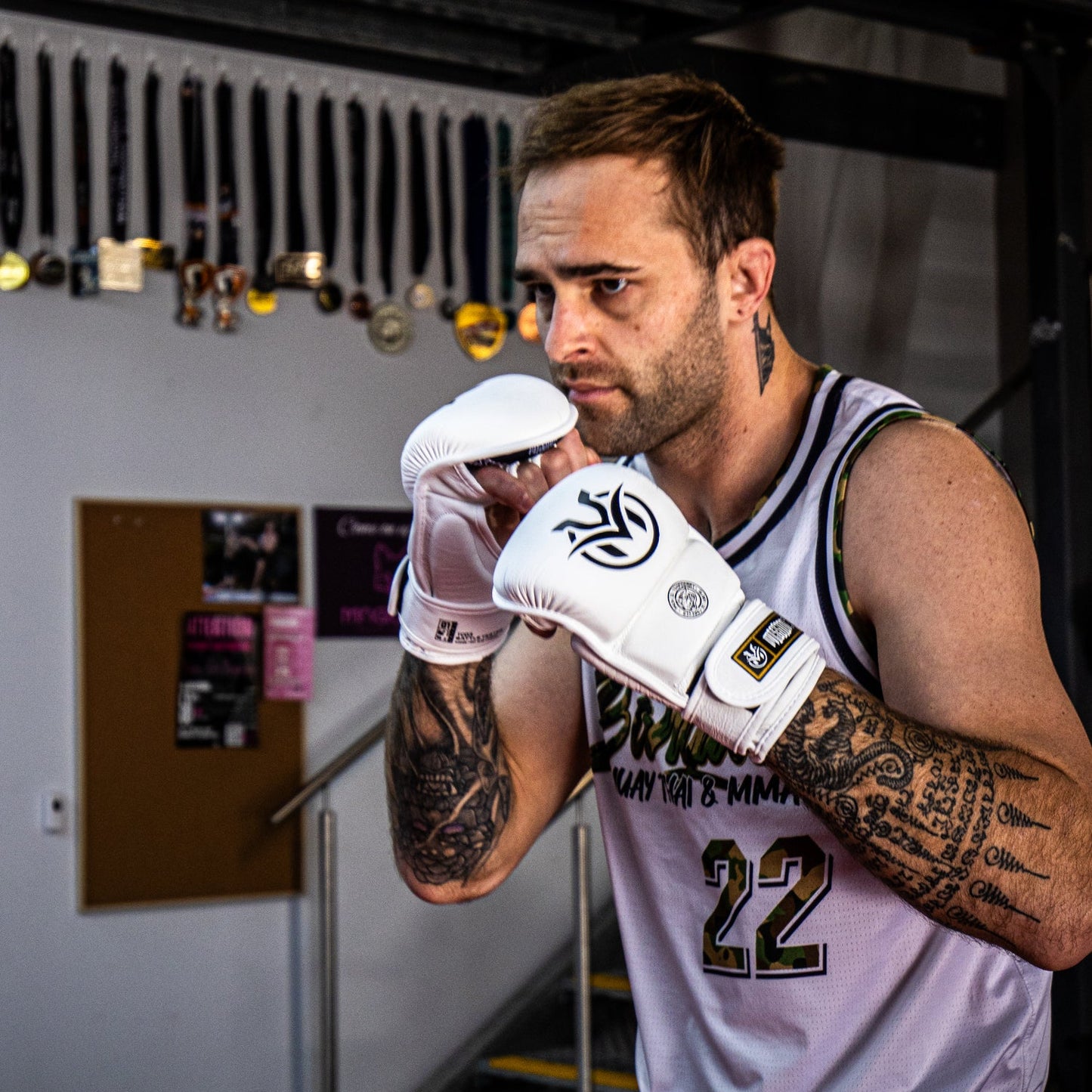 Man wearing white MMA gloves and a sports jersey in a gym setting